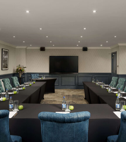 Elegant conference room setup with tables, green apples, and water bottles for a welcoming meeting.