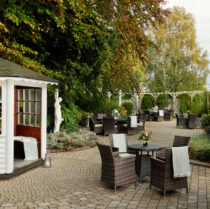 Guests enjoy leisurely afternoon in a charming outdoor patio with tables, chairs, and lush greenery.
