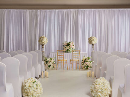 Elegant hotel wedding setup with floral decor and candlelit aisle.