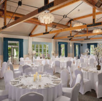 Elegant hotel banquet hall with round tables and white chairs set for an event.