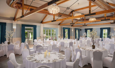 Elegant hotel banquet hall with round tables and white chairs set for an event.
