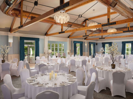 Elegant hotel banquet hall with round tables and white chairs set for an event.