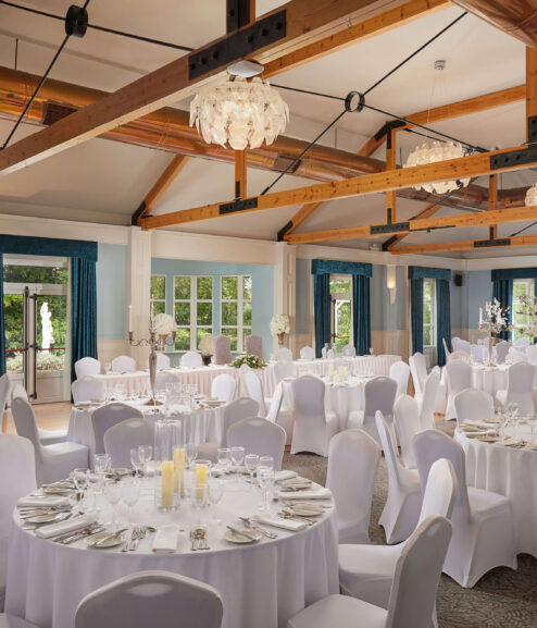 Elegant hotel banquet hall with round tables and white chairs set for an event.