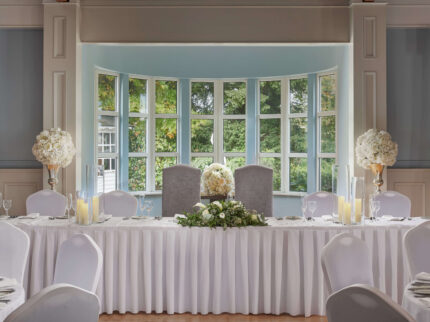 Elegant wedding table setup with flowers in a bright, serene room with large windows.
