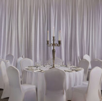 Elegant banquet hall set for guests with round tables, floral centrepieces, and candlelight.