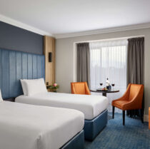 Cosy hotel room with twin beds, a table with wine, and welcoming decor for a relaxing stay.