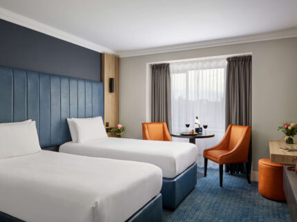 Cosy hotel room with twin beds, a table with wine, and welcoming decor for a relaxing stay.