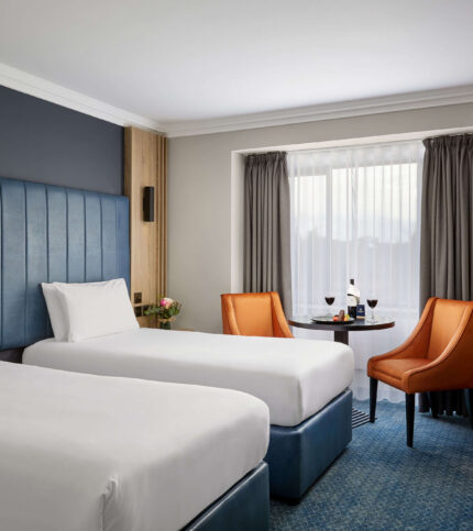 Cosy hotel room with twin beds, a table with wine, and welcoming decor for a relaxing stay.