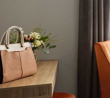 Elegant hotel room with warm lighting, a leather bag on the wooden desk, and an orange chair.