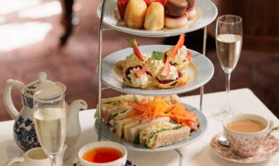 Afternoon tea set with tiered tray, scones, sandwiches, and tea on elegant table.