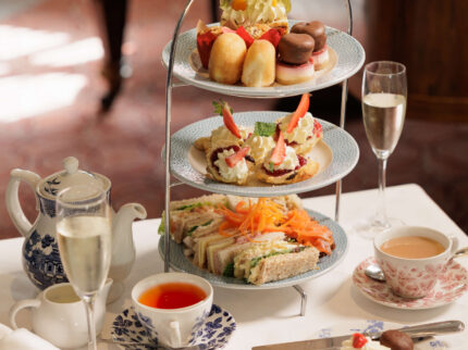 Afternoon tea set with tiered tray, scones, sandwiches, and tea on elegant table.