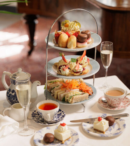 Afternoon tea set with tiered tray, scones, sandwiches, and tea on elegant table.