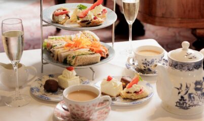Elegant afternoon tea setup with pastries, sandwiches, and tea, in a cosy hotel setting.