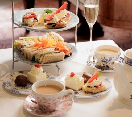Elegant afternoon tea setup with pastries, sandwiches, and tea, in a cosy hotel setting.