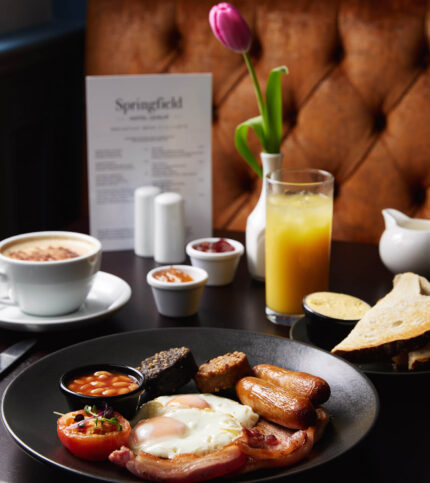 A warm, inviting breakfast setting at Springfield Hotel with a full English breakfast, drinks, and a menu.