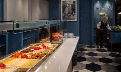 Elegant hotel buffet with assorted dishes and staff preparing tables in a welcoming setting.