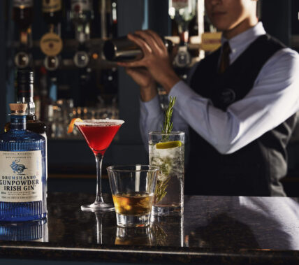A hotel bartender mixes drinks for guests at a cosy, elegant bar featuring cocktails.