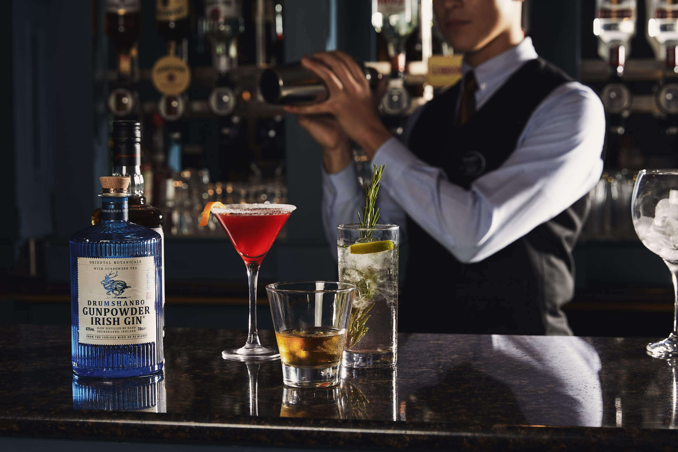 A hotel bartender mixes drinks for guests at a cosy, elegant bar featuring cocktails.