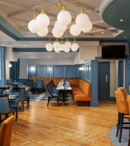 Elegant hotel dining area with blue walls, warm lighting, and inviting orange seating.