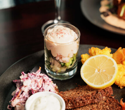 Gourmet dish with salad, fried fish, and a lemon slice, next to a glass of white wine.