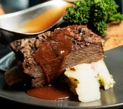 Tender beef rib with rich gravy, served on creamy mashed potatoes with a fresh garnish.