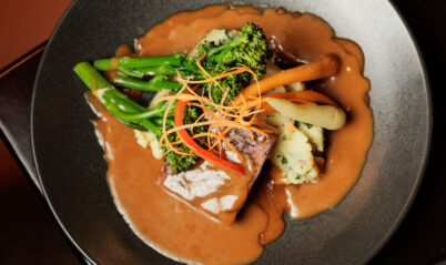 Gourmet meal with vegetables and gravy on a dark plate at Springfield Hotel restaurant.