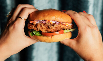 Hands holding a gourmet burger with fresh lettuce and tomato.