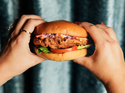 Hands holding a gourmet burger with fresh lettuce and tomato.