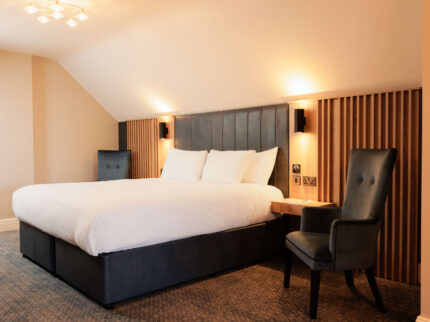 Spacious hotel room with a cosy king-sized bed, warm lighting, and elegant seating for relaxation.