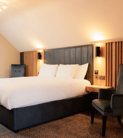 Spacious hotel room with a cosy king-sized bed, warm lighting, and elegant seating for relaxation.