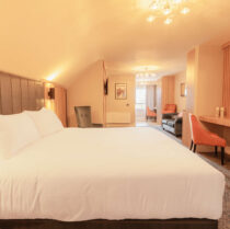 Spacious hotel room with cosy lighting, large bed, seating area, and open window.