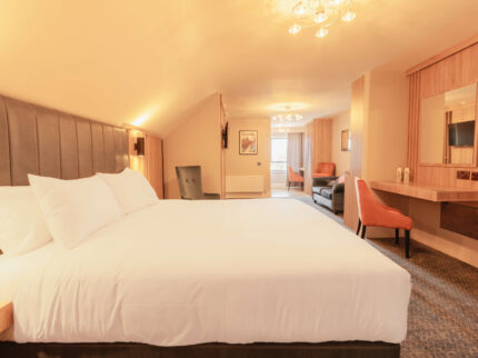 Spacious hotel room with cosy lighting, large bed, seating area, and open window.