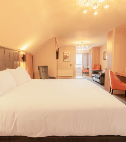 Spacious hotel room with cosy lighting, large bed, seating area, and open window.