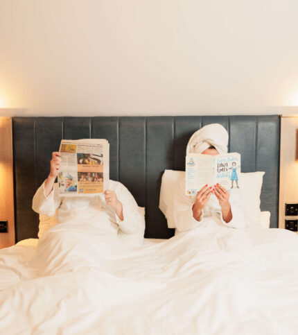 Couple in bathrobes reading in cosy hotel room.