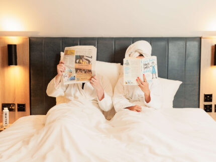 Couple in bathrobes reading in cosy hotel bed, Springfield Hotel.