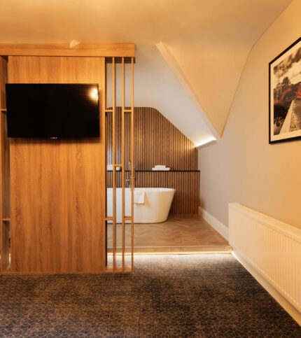Elegant hotel room with a freestanding bathtub and wall-mounted TV, creating a cosy retreat.