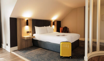 Cosy hotel room with double bed and a bright yellow suitcase.