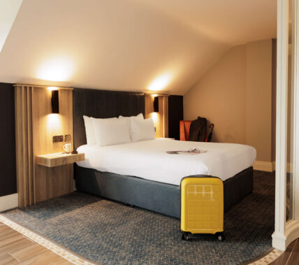 Cosy hotel room with double bed and a bright yellow suitcase.