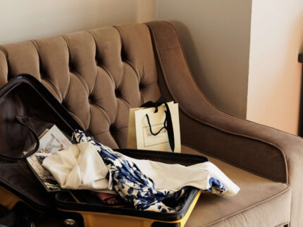 Open suitcase and shopping bag on a cosy hotel sofa.