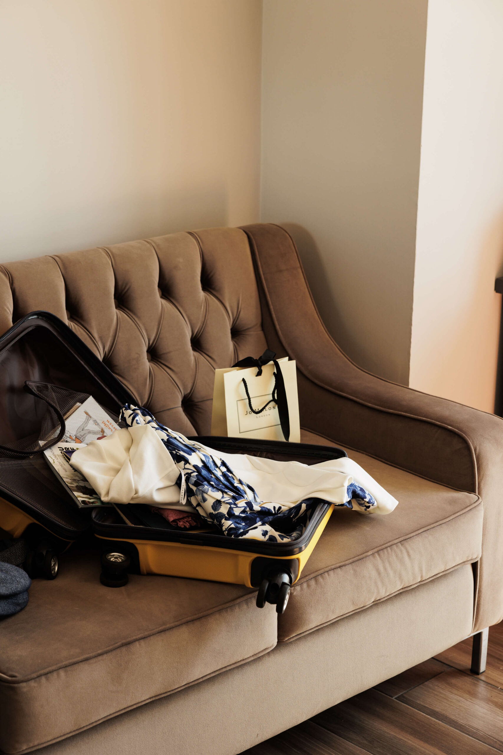 Open suitcase and shopping bag on a cosy hotel sofa.