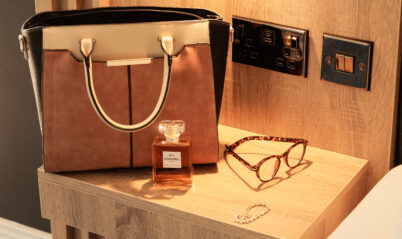 Luxurious hotel room nightstand with handbag, perfume, and glasses.