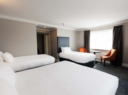 Spacious hotel room with three beds and cosy seating area.