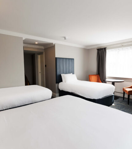 Spacious hotel room with three beds and cosy seating area.