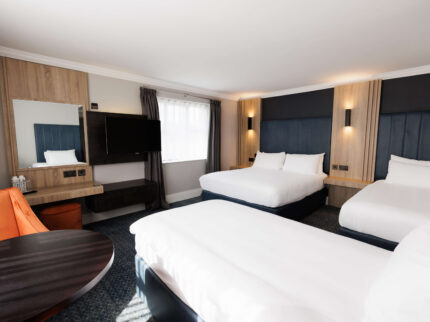 Spacious hotel room with three beds, a sitting area, and a large window.