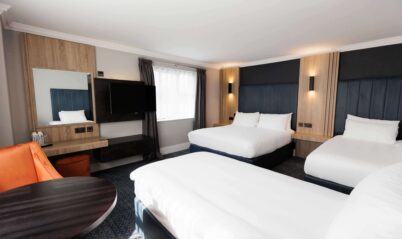 Bright hotel room with two double beds, modern décor, TV, and a cosy seating area.