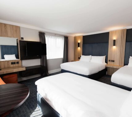 Bright hotel room with two double beds, modern décor, TV, and a cosy seating area.