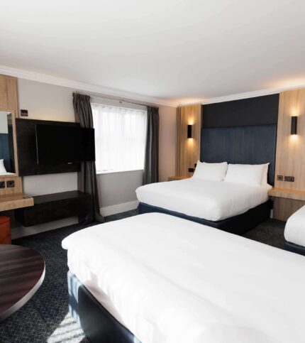 Bright hotel room with two double beds, modern décor, TV, and a cosy seating area.