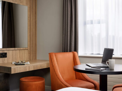 Cosy hotel room with table, laptop, and comfortable chairs by a window.