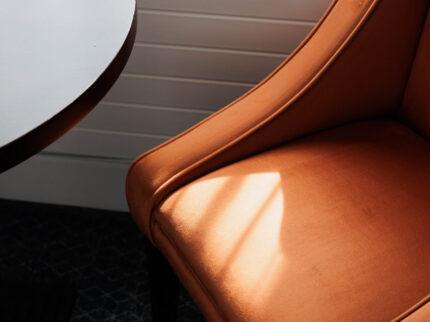 Warm sunlit corner with an orange armchair and round table in Springfield Hotel room.