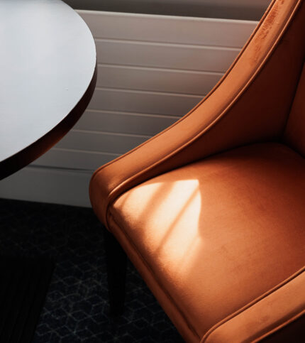 Warm sunlit corner with an orange armchair and round table in Springfield Hotel room.